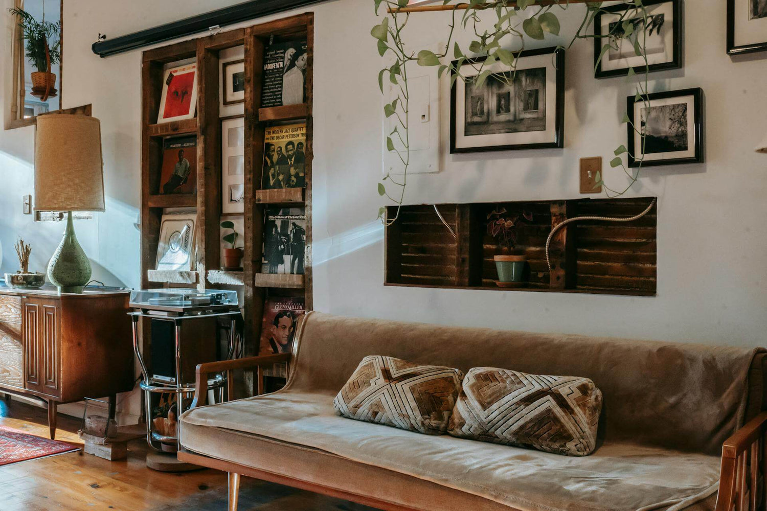 Small space urban living room with a brown sofa, wooden bookshelf, and framed pictures on the wall.